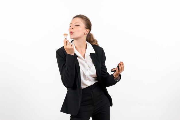 Vista frontal mujer joven en traje clásico estricto haciendo su maquillaje en el escritorio blanco mujer trabajo traje negocio serio