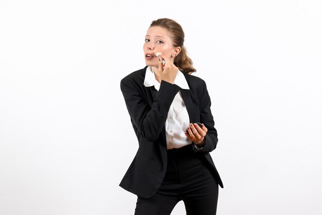 Vista frontal mujer joven en traje clásico estricto haciendo su maquillaje sobre fondo blanco claro trabajo de mujer traje de trabajo trabajo femenino