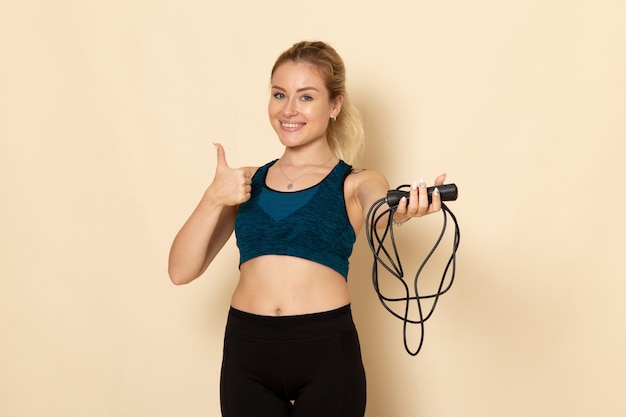 Vista frontal mujer joven en traje deportivo sosteniendo cuerdas en la pared blanca luz salud belleza entrenamiento cuerpo deporte