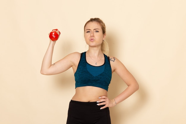 Vista frontal mujer joven en traje deportivo sosteniendo pesas rojas en la pared blanca mujer de entrenamiento de belleza de salud corporal de deporte