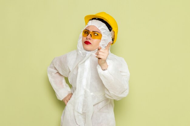 Vista frontal mujer joven en traje especial blanco y casco amarillo amenazando con el dedo en el trabajo del espacio verde