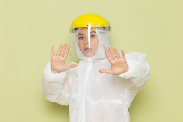 Vista frontal mujer joven en traje especial blanco y casco amarillo posando con precaución en la ciencia uniforme del traje espacial verde