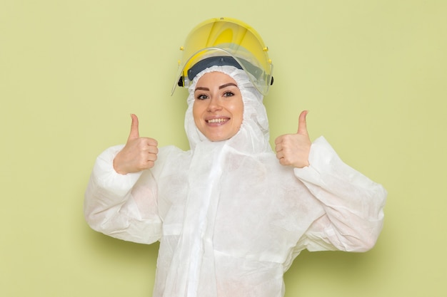 Vista frontal mujer joven en traje especial blanco y casco amarillo posando con una sonrisa en el trabajo de ciencia uniforme de traje espacial verde