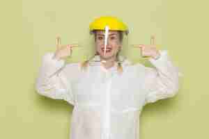 Foto gratuita vista frontal mujer joven en traje especial blanco y casco amarillo sonriendo en el trabajo del espacio verde