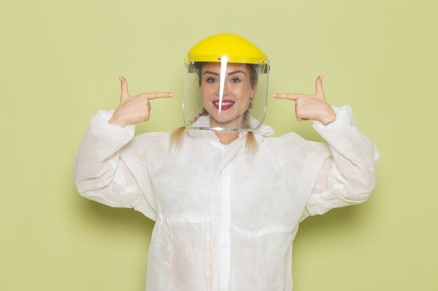 Vista frontal mujer joven en traje especial blanco y casco amarillo sonriendo en el trabajo del espacio verde