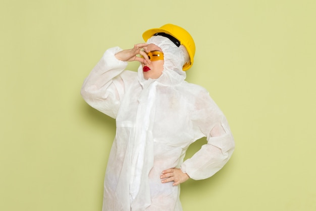 Foto gratuita vista frontal mujer joven en traje especial blanco y casco amarillo tapándose la nariz en el espacio verde