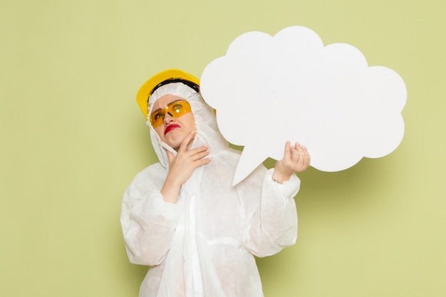 Vista frontal mujer joven en traje especial blanco y casco protector amarillo con enorme cartel blanco en la ciencia uniforme del traje espacial verde