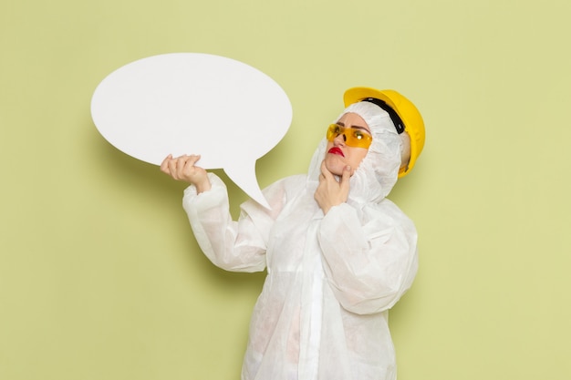 Vista frontal mujer joven en traje especial blanco y casco protector amarillo con enorme cartel blanco en el espacio verde