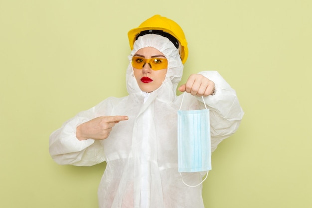 Vista frontal mujer joven en traje especial blanco y casco protector amarillo con máscara estéril en la ciencia uniforme del traje espacial verde