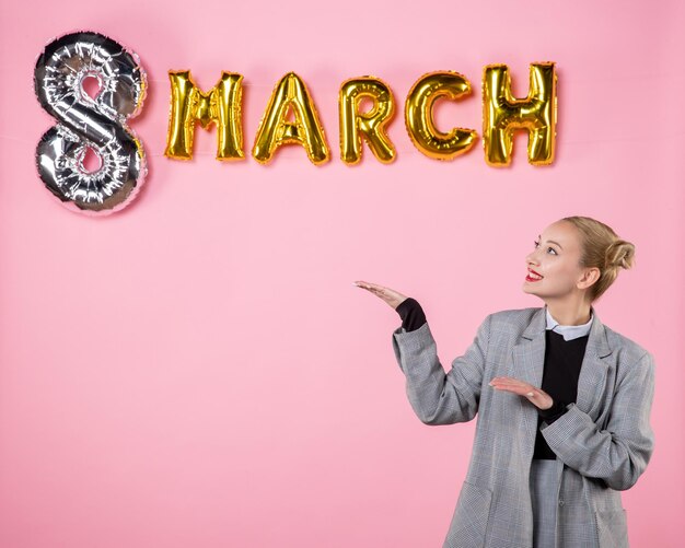 Vista frontal mujer joven en traje gris con decoración de marzo sobre fondo rosa igualdad vacaciones color día de la mujer fiesta mujer sensual presente