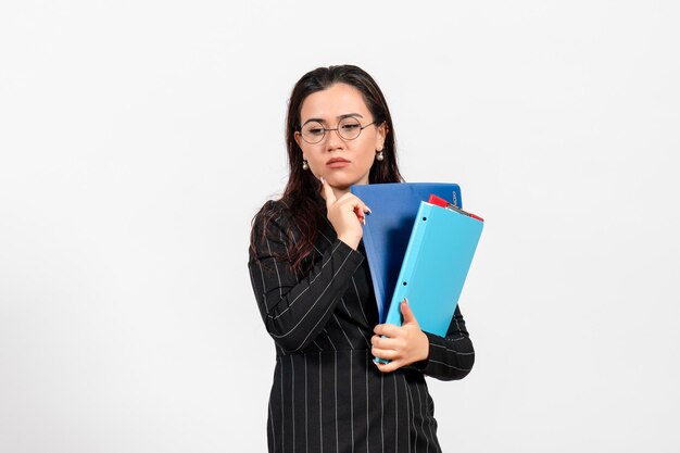 Vista frontal mujer joven en traje oscuro estricto sosteniendo documentos con rostro estresado sobre fondo blanco trabajo de oficina de negocios de documentos femeninos