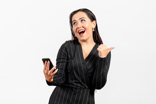 Vista frontal mujer joven en traje oscuro estricto sosteniendo teléfono sobre fondo blanco mujer dama moda oficina trabajador trabajo belleza