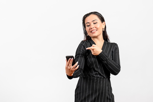 Vista frontal mujer joven en traje oscuro estricto sosteniendo teléfono sobre fondo blanco mujer dama moda oficina trabajador trabajo belleza
