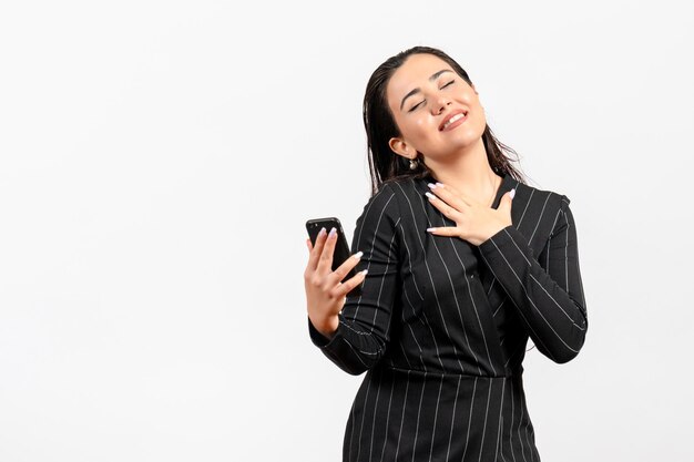 Vista frontal mujer joven en traje oscuro estricto sosteniendo teléfono sobre fondo blanco mujer dama moda trabajador trabajo belleza