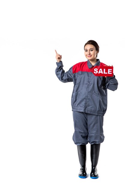 Vista frontal de la mujer joven en uniforme con placa de venta roja sobre pared blanca