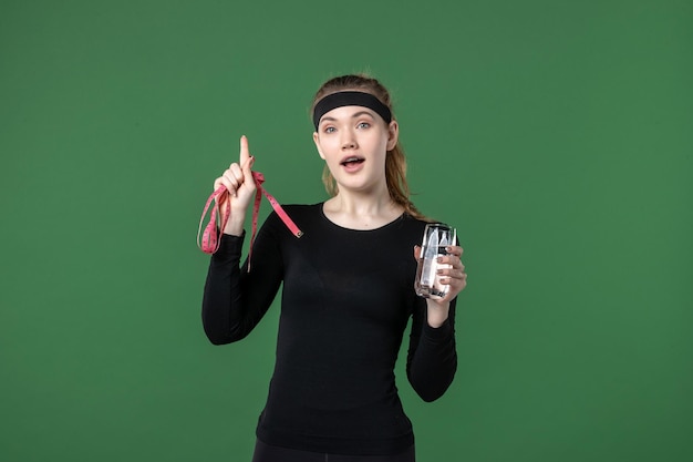 Vista frontal mujer joven con vaso de agua y medida de cintura sobre fondo verde deporte atleta mujer entrenamiento color de cuerpo negro