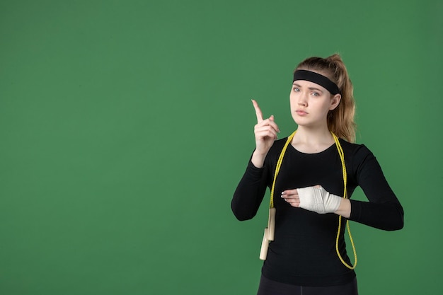 Vista frontal mujer joven con vendaje alrededor de su brazo herido sobre fondo verde atleta entrenamiento dolor salud mujer lesión deporte cuerpo hospital triste