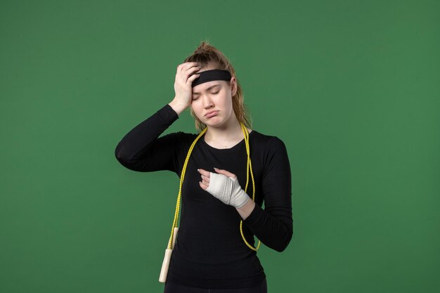 Vista frontal mujer joven con vendaje alrededor de su brazo herido sobre fondo verde deporte atleta dolor lesión mujer entrenamiento color de cuerpo