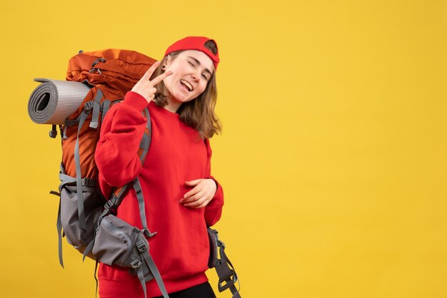 Vista frontal mujer joven viajero en mochila roja gesticulando el signo de la victoria