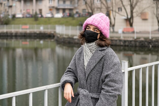 Vista frontal de la mujer con máscara médica en la ciudad junto al lago