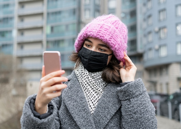 Vista frontal de la mujer con máscara médica en la ciudad tomando selfie