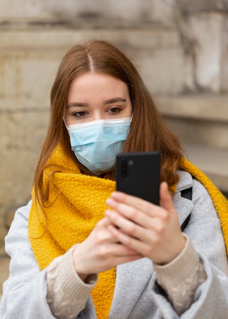 Vista frontal de la mujer con máscara médica tomando fotografías con smartphone