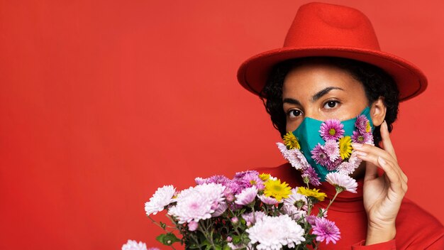 Vista frontal de la mujer con máscara posando con flores