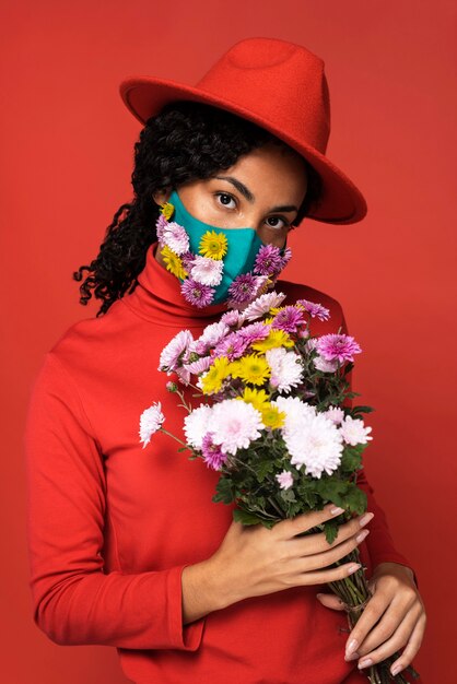 Vista frontal de la mujer con máscara y ramo de flores