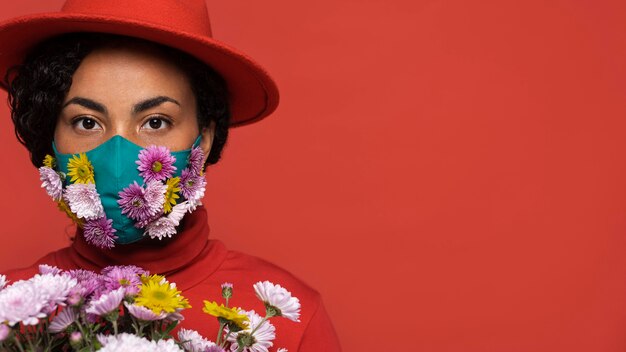 Vista frontal de la mujer con máscara con ramo de flores