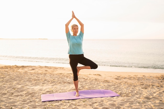 Vista frontal de la mujer mayor haciendo yoga en la playa