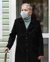 Foto gratuita vista frontal de la mujer mayor con máscara médica y bastón