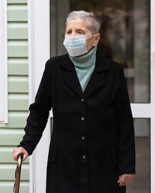 Vista frontal de la mujer mayor con máscara médica y bastón