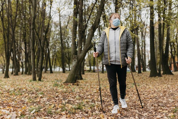 Vista frontal de la mujer mayor con máscara médica y bastones de trekking