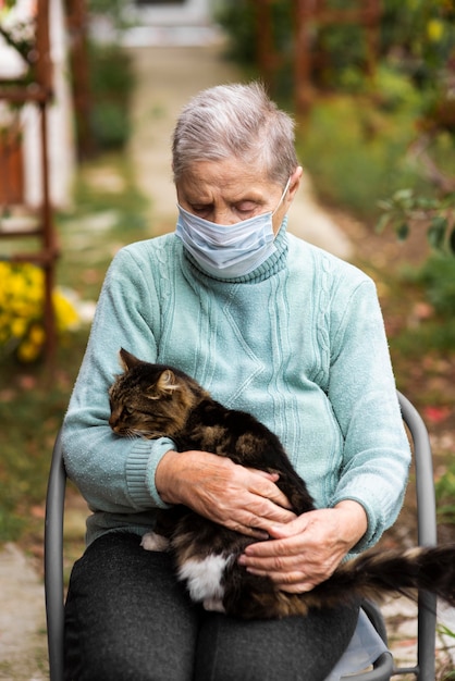 Vista frontal de la mujer mayor con máscara médica y gato en el hogar de ancianos