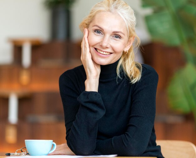 Vista frontal de la mujer mayor sonriente posando mientras toma un café