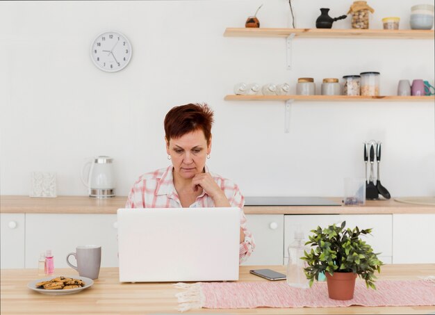 Vista frontal de la mujer mayor en su casa en su computadora portátil