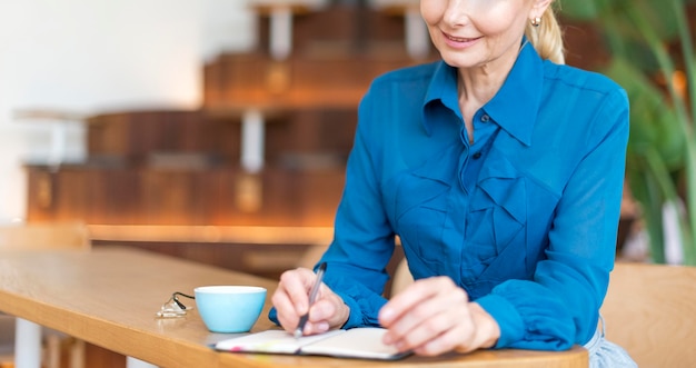 Vista frontal de la mujer mayor trabajando mientras toma café
