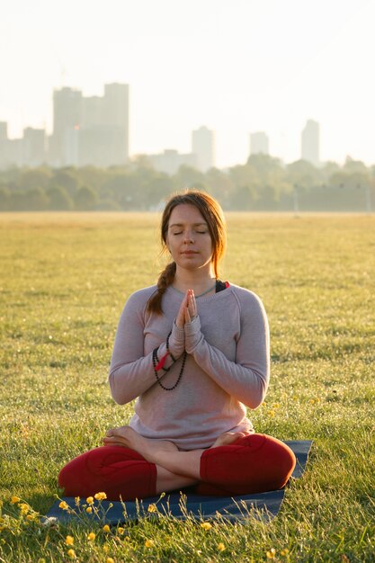 Vista frontal de la mujer meditando al aire libre en la estera de yoga