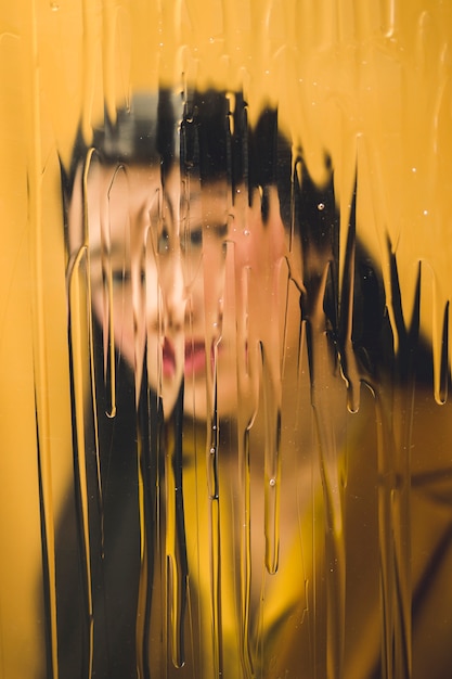 Vista frontal de una mujer mirando a la cámara detrás de una ventana mojada