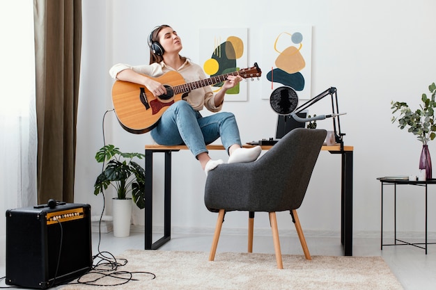 Vista frontal de la mujer músico en casa tocando la guitarra acústica y cantando