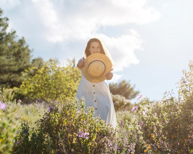 Vista frontal de la mujer en la naturaleza posando mientras sostiene el sombrero