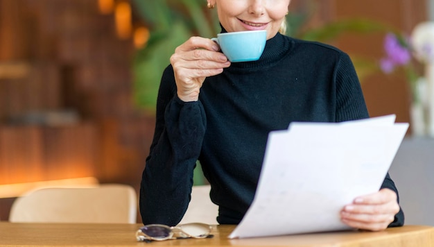 Vista frontal de la mujer de negocios mayor leyendo papeles mientras toma café