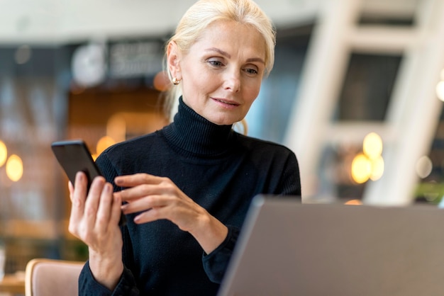 Vista frontal de la mujer de negocios mayor que trabaja en la computadora portátil y el teléfono inteligente