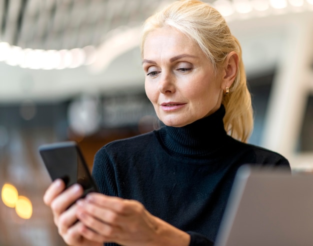 Vista frontal de la mujer de negocios mayor que trabaja en la computadora portátil y el teléfono inteligente