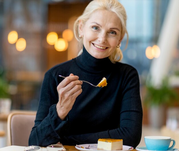 Vista frontal de la mujer de negocios mayor sonriente con postre mientras trabaja