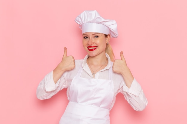 Vista frontal mujer pastelera en ropa blanca sonriendo y posando en la pared rosa cocinar confitería trabajo de pastelería dulce