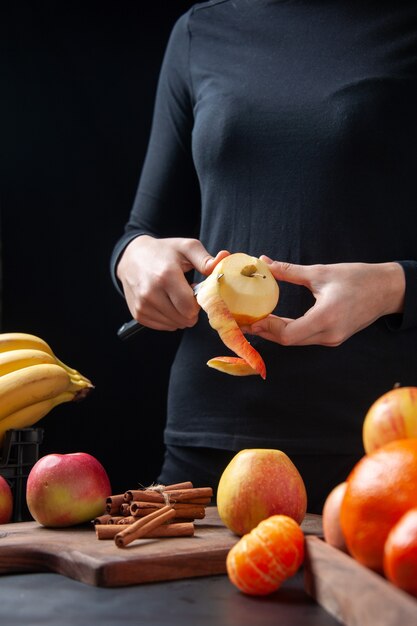 Vista frontal mujer pelando manzana fresca con cuchillo en la mesa de la cocina