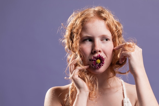Vista frontal de la mujer pelirroja posando con un crisantemo en la boca y copia espacio