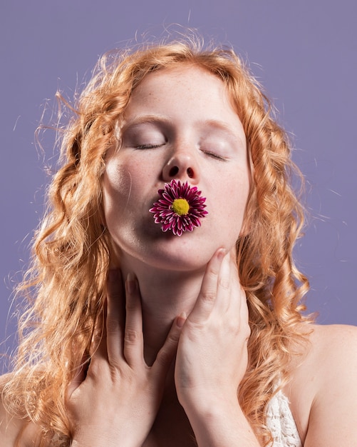 Vista frontal de la mujer pelirroja posando con un crisantemo en la boca