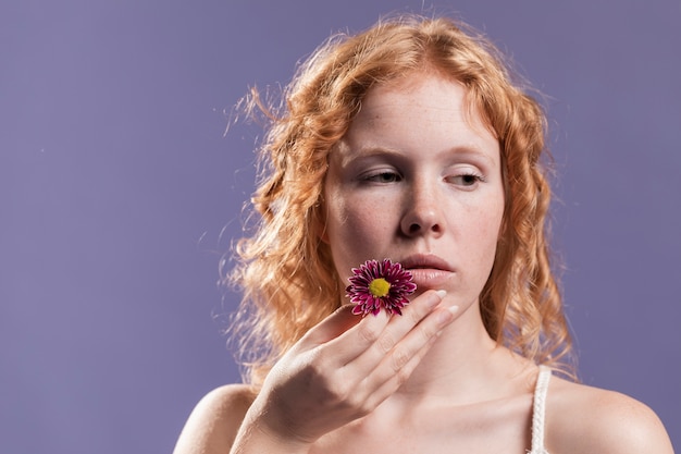 Foto gratuita vista frontal de la mujer pelirroja sosteniendo una flor cerca de su boca con espacio de copia